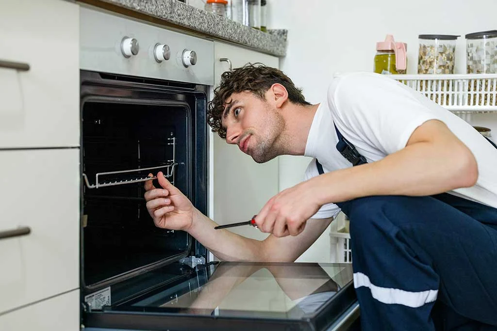 Appliance technician inspecting an oven with a screwdriver